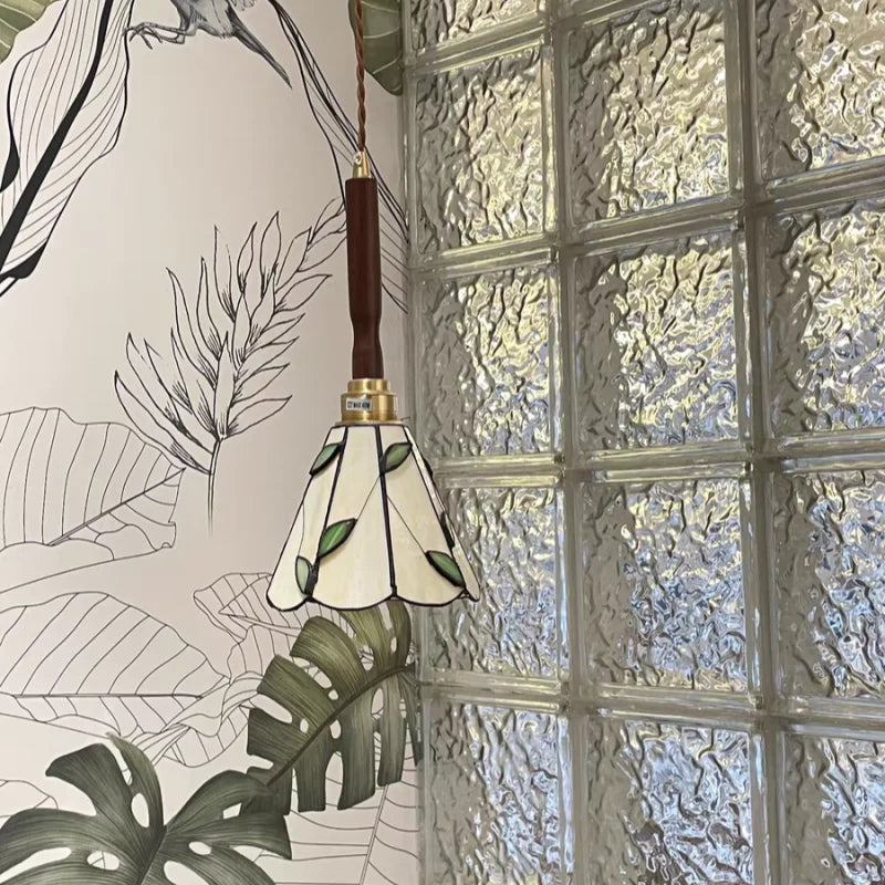 Pendant light with leaf-patterned shade against a glass block wall and leafy background