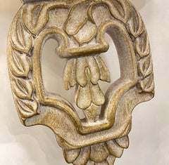 Decorative metal knocker with floral design on a beige background.