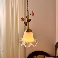 A pendant light with a clear fluted glass shade and a brass stem featuring pink ceramic roses and green leaves, illuminated warmly.