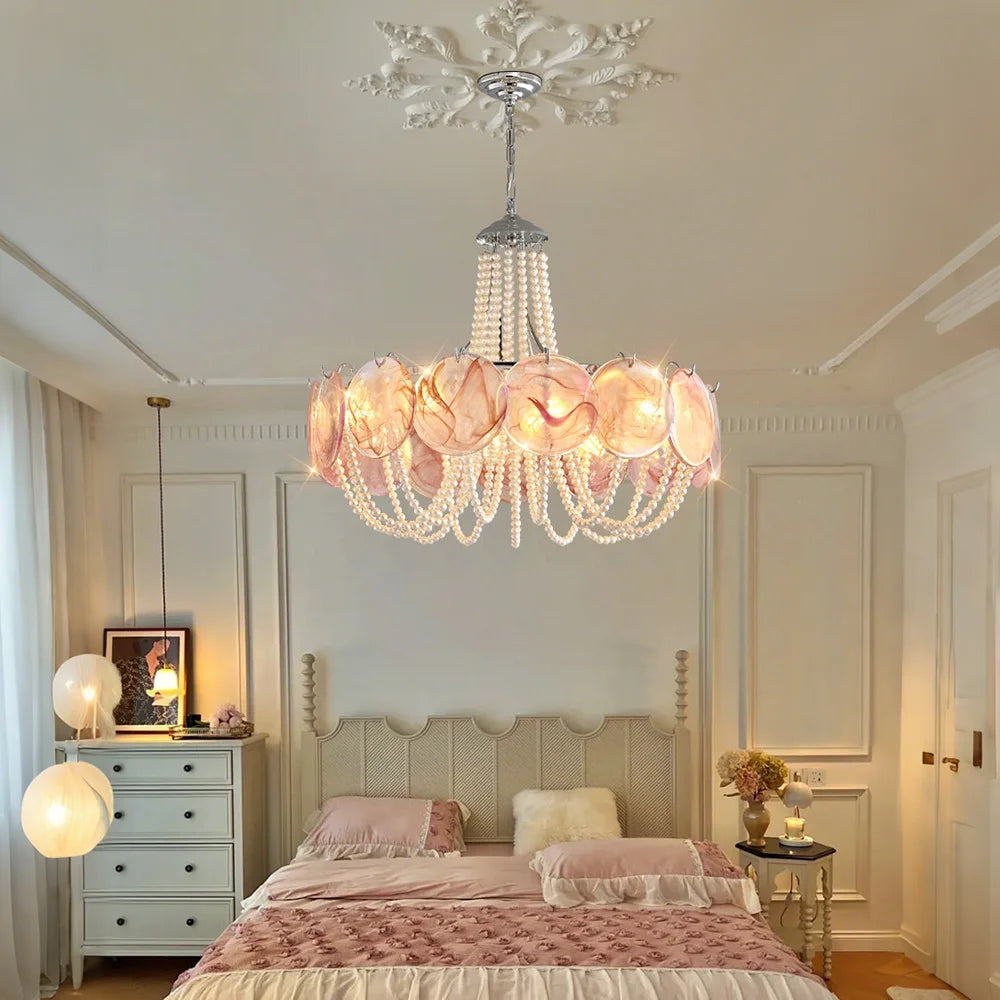 A pink glass beaded chandelier with pearl strings, hanging above a bed in a softly lit bedroom.