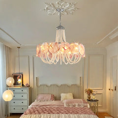 A pink glass beaded chandelier with pearl strings, hanging above a bed in a softly lit bedroom.