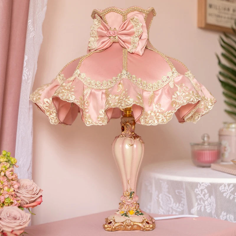 Pink and gold decorative lamp with a lace shade on a table.