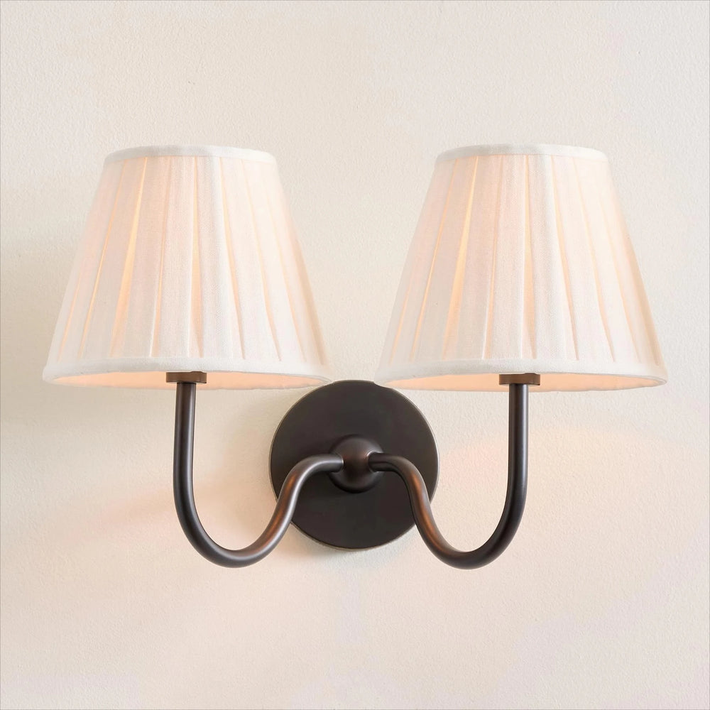 Wall-mounted light fixture with two lampshades on a plain wall.