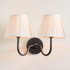 Wall-mounted light fixture with two lampshades on a plain wall.