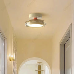 A modern flush mount ceiling light with a white base and a clear diffuser with a red accent, illuminating a hallway with arched doorways.