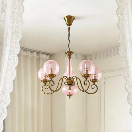 A gold-finished pendant light with pink glass globes hanging from the ceiling, framed by white lace curtains.