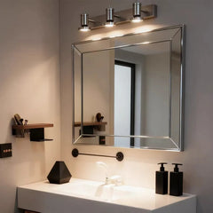 A bathroom vanity area featuring a silver wall sconce with three adjustable LED heads mounted above a large mirror.