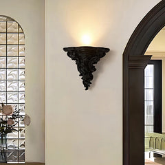 Small black ornate resin wall sconce mounted on a white wall, casting light upwards.