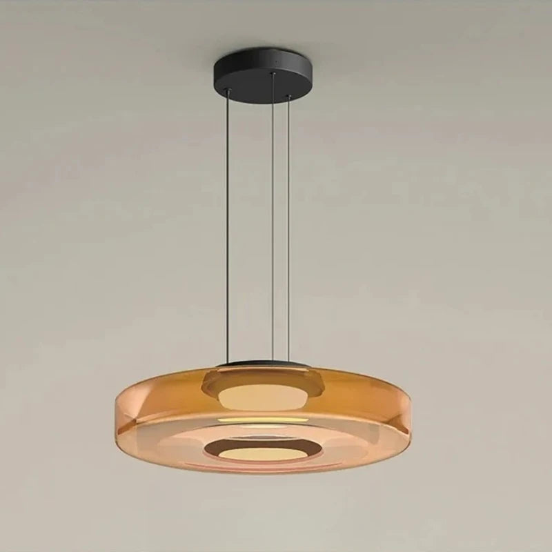 Amber glass disk pendant light with a black ceiling mount and cord.