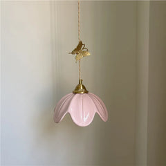 Pink ceramic petal pendant light with a brass butterfly accent hanging against a white wall.
