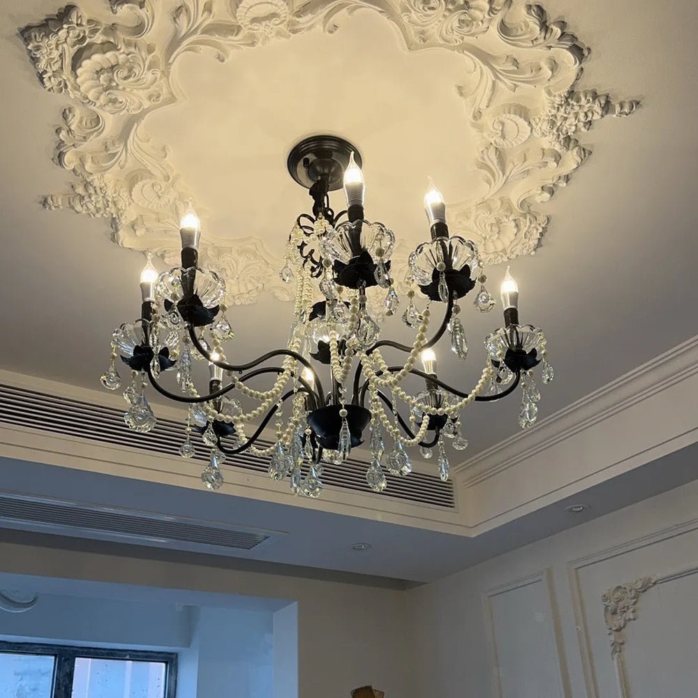 View of a black candelabra chandelier with crystal and pearl embellishments installed in a room with ornate ceiling molding.