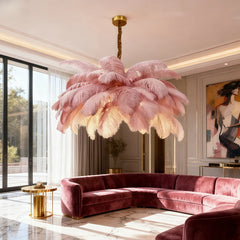 Pink feather chandelier with gold accents hanging in a modern living room above a velvet sectional sofa.