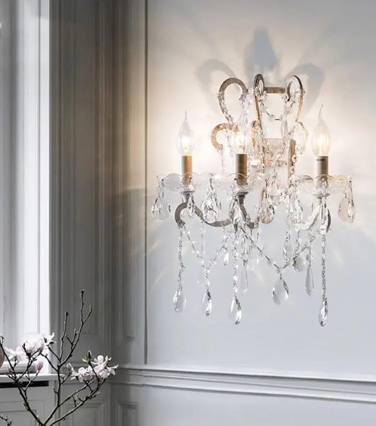Crystal wall sconce with three lights on a white wall.