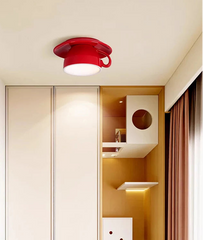 A red ceramic coffee cup semi-flush mount light fixture installed on a ceiling in a modern room with built-in shelving.