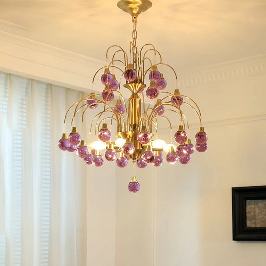 Gold chandelier with cascading purple droplet crystals and polished finish.
