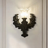 Black resin wall sconce with ornate detailing and a fluted glass shade, mounted on a white wall.