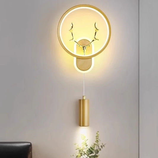 Gold wall sconce with circular LED halo and integrated antler design, with a hanging downlight cylinder.