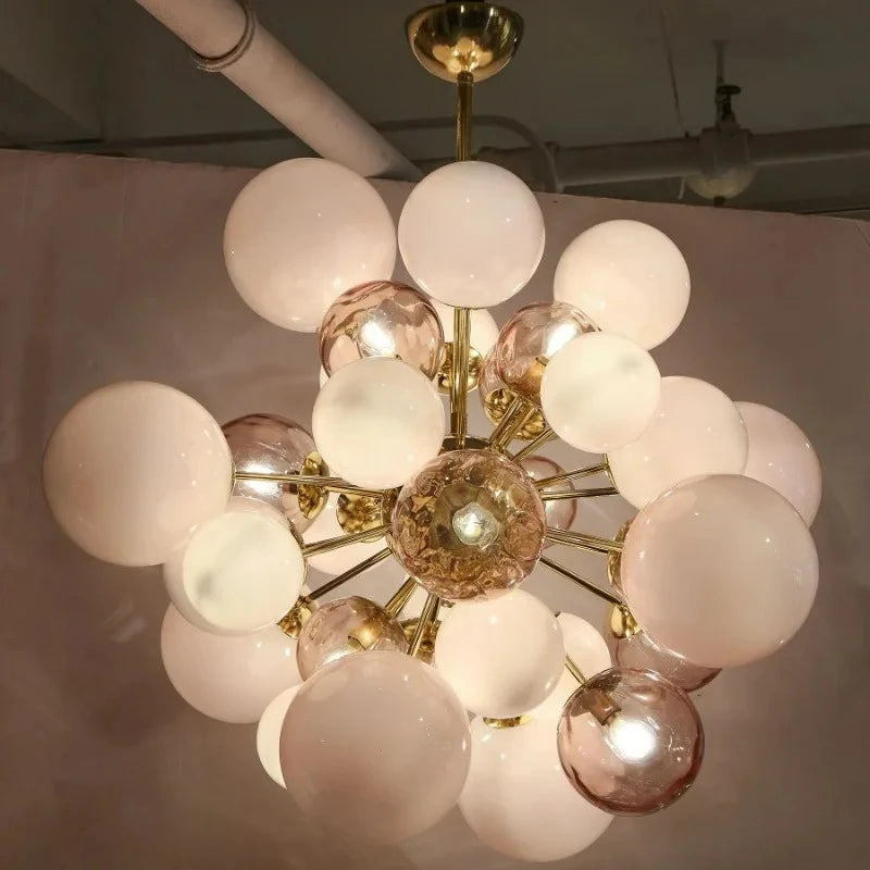 Illuminated gold glass ball cluster pendant light with frosted and clear orbs against a grey wall.