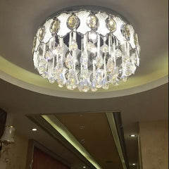 The chrome and crystal tiered chandelier installed in a modern room with a high ceiling, showcasing its illumination and design.