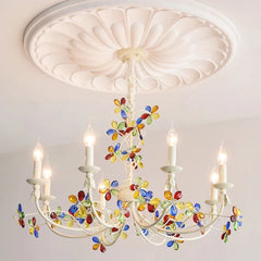 A white candelabra-style chandelier featuring numerous colorful crystal flower embellishments and lit candle bulbs.