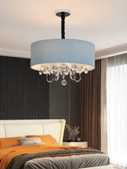 A bedroom setting with a blue fabric drum pendant light illuminating the space above the bed.