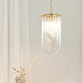 Close-up of a single gold U-shaped pendant light with clear glass tubes hanging from a chain against a white curtain background.