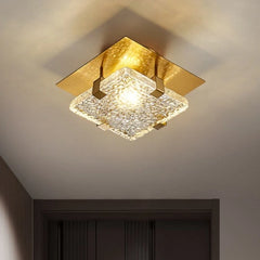 A square gold flush mount ceiling light with faceted crystal diffuser, casting light onto a ceiling.