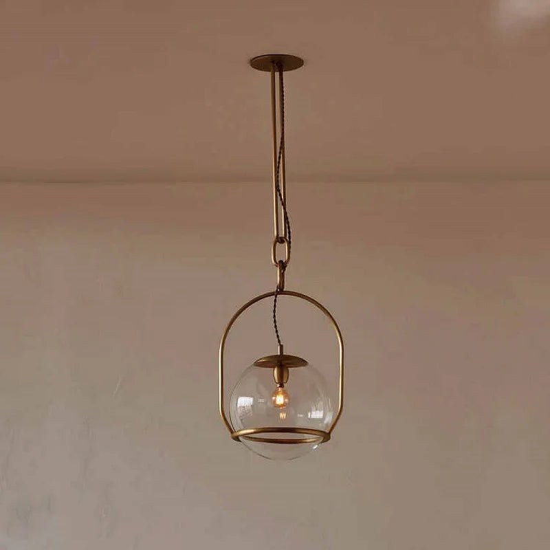 A black metal frame surrounds a clear glass globe pendant light, suspended by a chain from a ceiling mount.