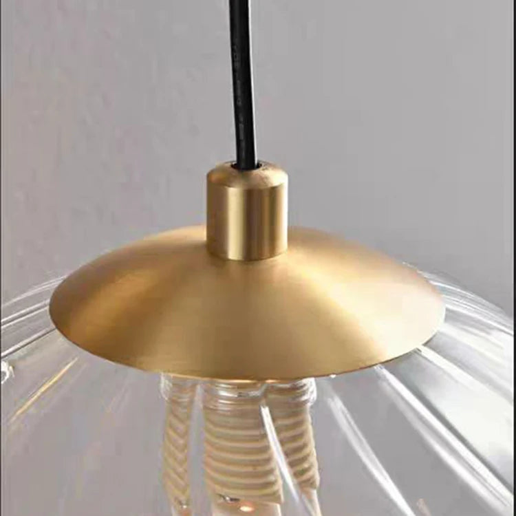 Close-up of a gold pendant light fixture with a clear glass shade against a neutral background.