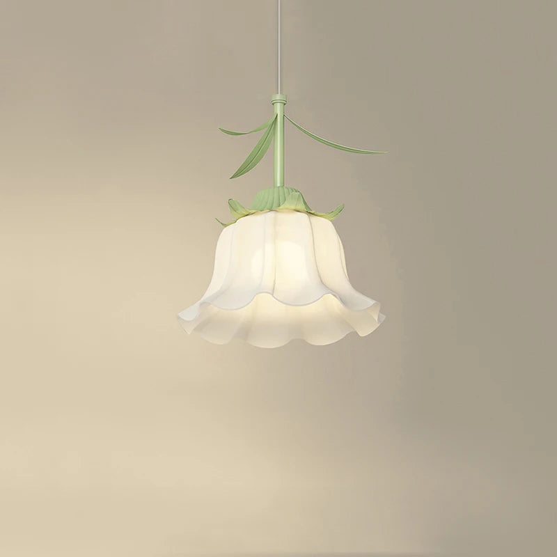 Close-up of a white frosted glass pendant light shaped like a flower bud with green stem and leaves, hanging against a cream-colored wall.