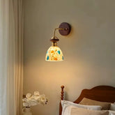 Wall sconce with a bell-shaped shade made of colorful shell fragments mounted on a wood base with a brushed gold arm.