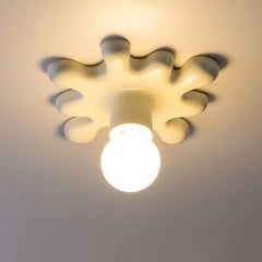 A white starburst shaped ceramic wall sconce with a light bulb, mounted on a ceiling.