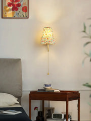 Decorative wall lamp with floral pattern on a neutral wall above a wooden side table.