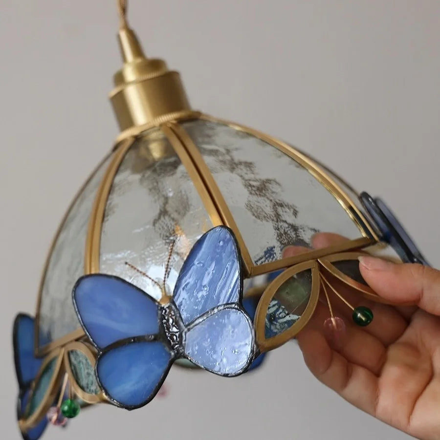 Decorative lamp with blue butterfly design held by a hand against a neutral background
