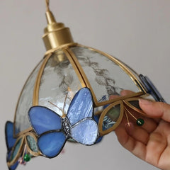 Decorative lamp with blue butterfly design held by a hand against a neutral background