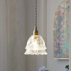 Small glass pendant light hanging against a neutral wall with floral decor.