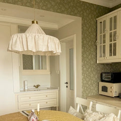 A white pleated fabric pendant light suspended over a round table in a room with green floral wallpaper.