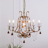 A vintage-style, multi-arm chandelier with a brushed gold finish, adorned with clear crystals and red fruit-shaped drops, and lit with five faux candle bulbs.
