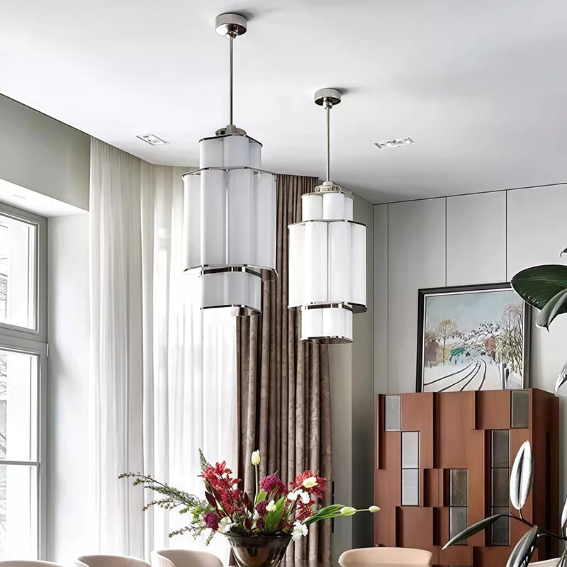 Two gold and white acrylic tiered pendant lights hanging in a dining room with a floral arrangement.