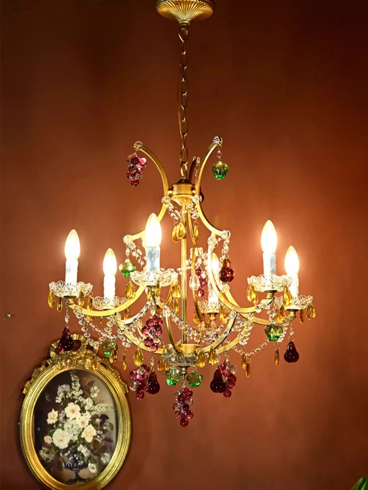 View of a gold chandelier with colorful crystal drops and an ornate frame, illuminated and set against a warm wall.