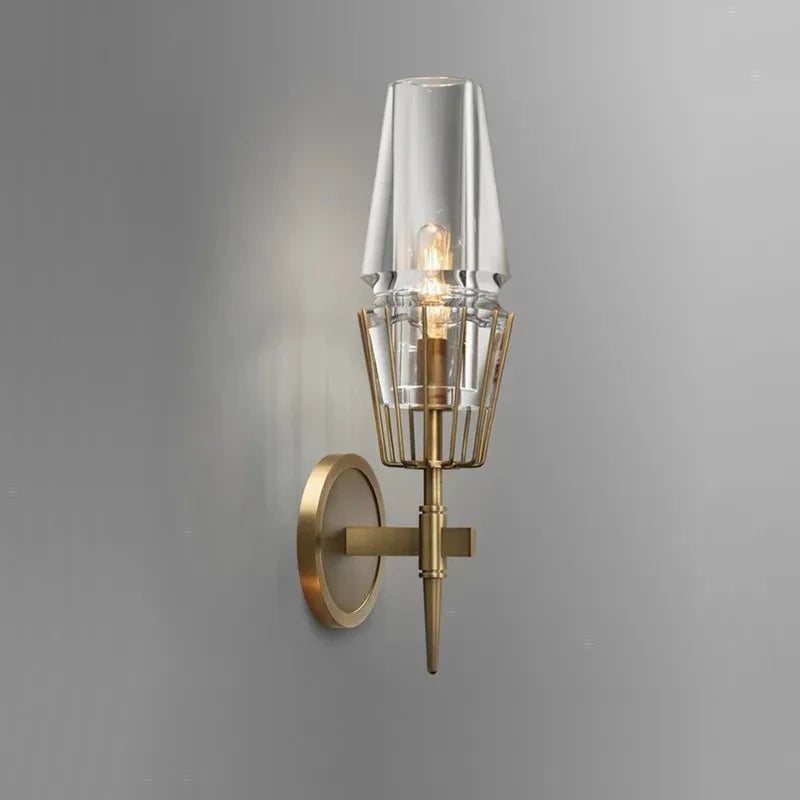 Single clear glass crystal wall sconce with a brushed gold frame mounted on a grey wall.