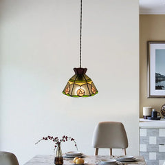 A glass floral pendant light with green and yellow accents hanging above a dining table.