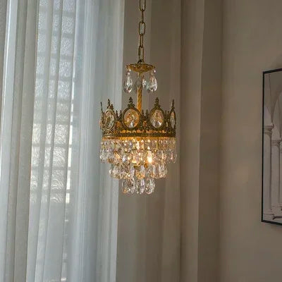 Decorative chandelier hanging in a room with light-colored walls and sheer curtains.