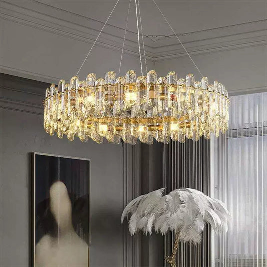 A large, circular gold chandelier adorned with numerous clear crystal teardrop-shaped elements, suspended from the ceiling in a well-lit room.