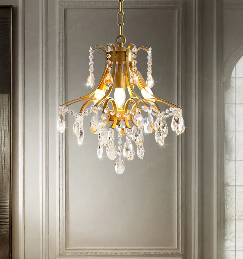 Gold chandelier with crystal accents hanging against a gray wall.