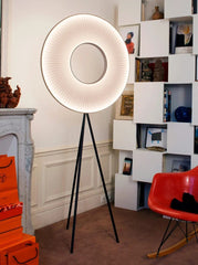 Modern floor lamp with a circular design in a room with a bookshelf and orange chair.