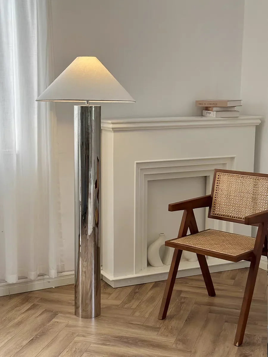 Floor lamp with a white shade in a room with wooden flooring and a fireplace.