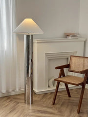 Floor lamp with a white shade in a room with wooden flooring and a fireplace.