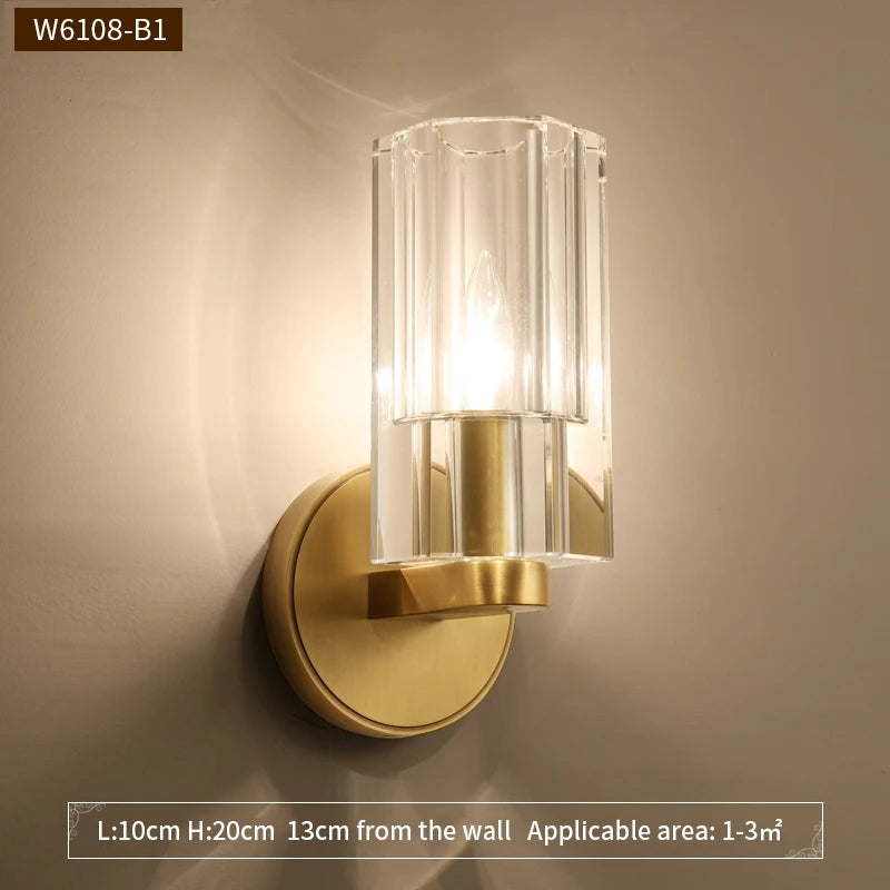 Wall-mounted light fixture with gold finish and clear glass shade on a beige wall.