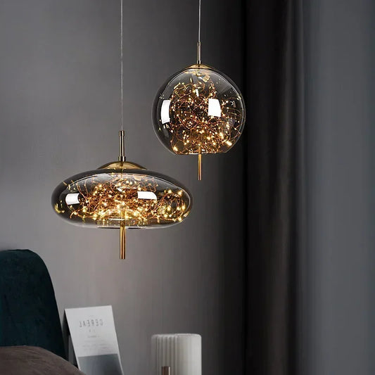 Two glass pendant lights with gold accents, filled with warm LED lights, hanging against a dark wall.
